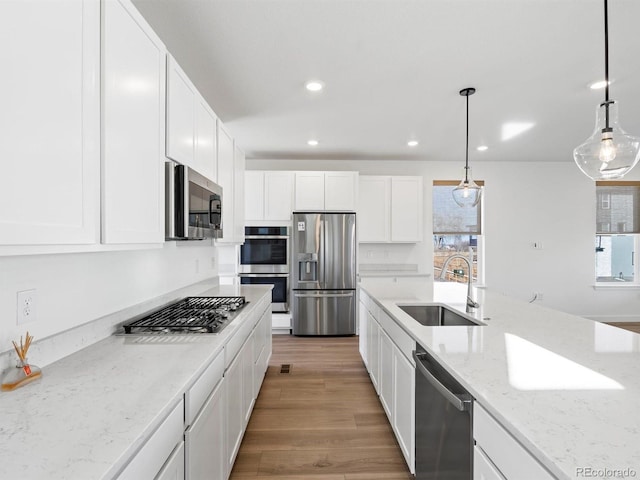 kitchen featuring light stone counters, stainless steel appliances, a sink, white cabinetry, and light wood-style floors