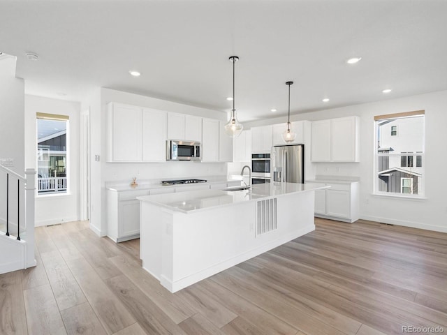 kitchen with a sink, white cabinets, appliances with stainless steel finishes, light wood finished floors, and an island with sink