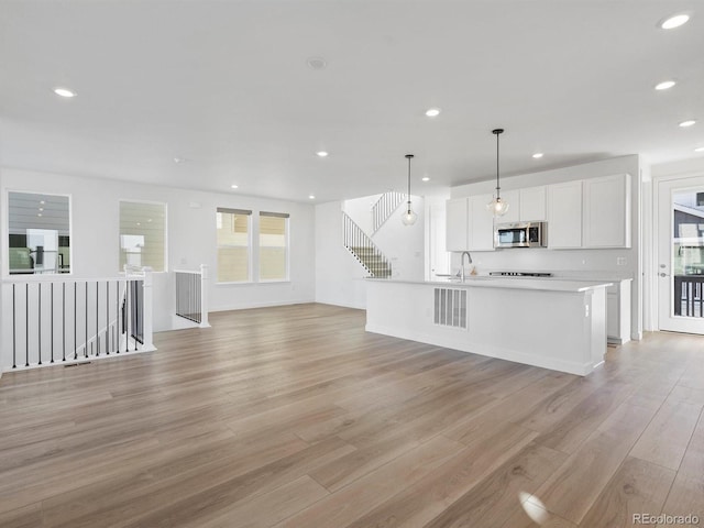 kitchen with light wood finished floors, white cabinets, stainless steel microwave, open floor plan, and recessed lighting