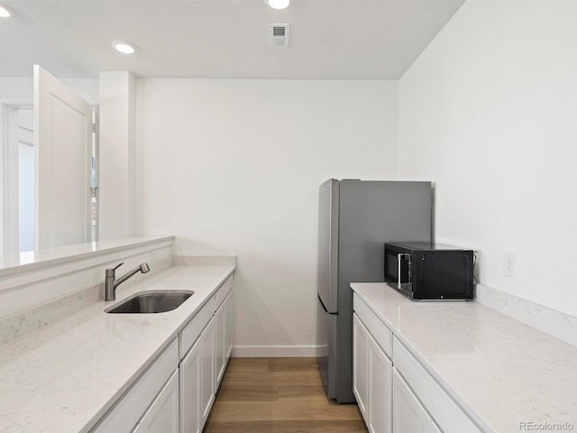 kitchen featuring visible vents, light wood-style floors, white cabinetry, a sink, and black microwave