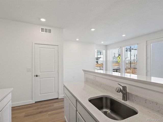 kitchen with light wood finished floors, visible vents, light stone counters, a sink, and recessed lighting