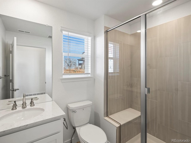 bathroom featuring toilet, vanity, a shower stall, and visible vents