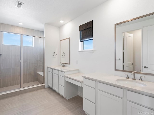 full bath with a shower stall, visible vents, two vanities, and a sink