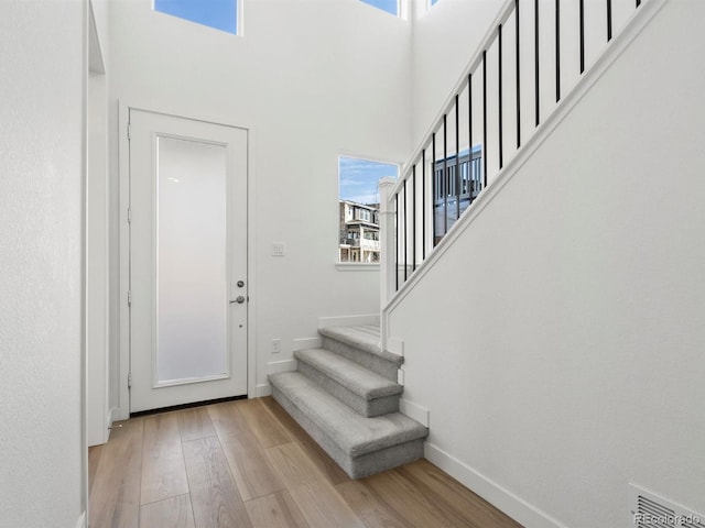 foyer featuring light wood-style floors, a high ceiling, baseboards, and stairs