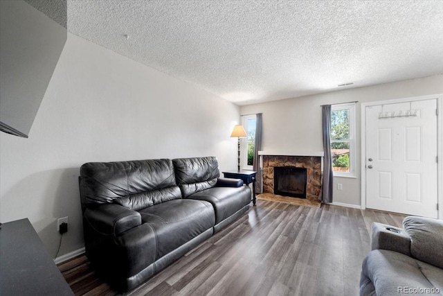 living room featuring a stone fireplace, a textured ceiling, and dark hardwood / wood-style floors