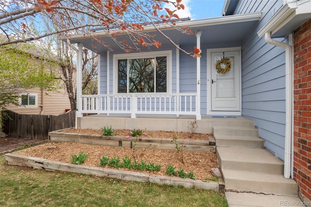 doorway to property with brick siding, a porch, and fence