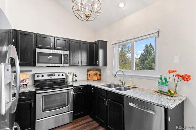 kitchen featuring dark cabinets, dark wood-style flooring, vaulted ceiling, stainless steel appliances, and a sink