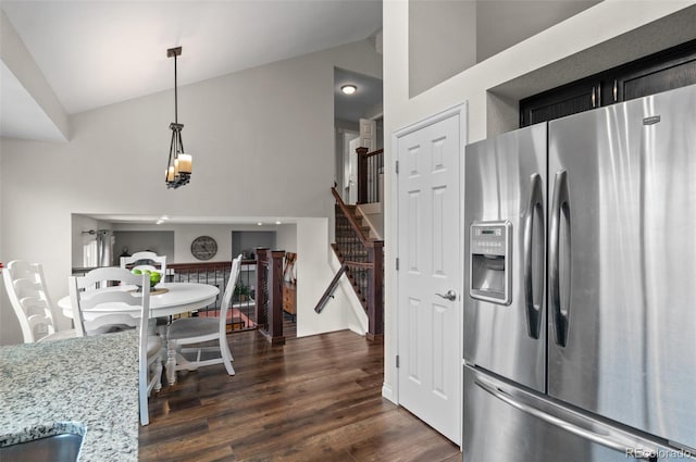 kitchen with pendant lighting, high vaulted ceiling, light stone countertops, dark wood-style flooring, and stainless steel fridge