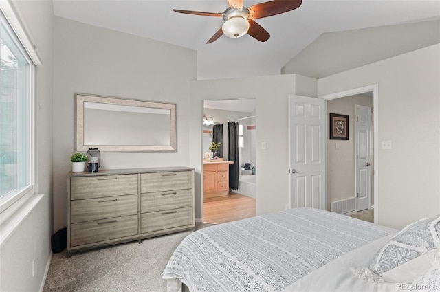 bedroom with ensuite bathroom, a ceiling fan, vaulted ceiling, visible vents, and light carpet