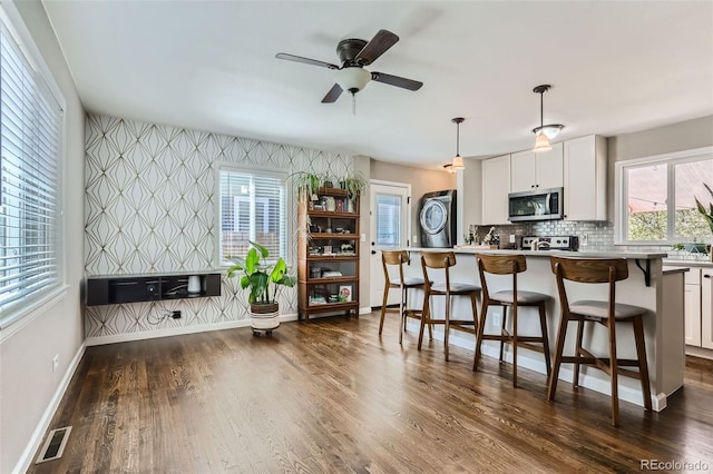 1171 Syracuse St, Denver, CO 80220 - kitchen featuring stainless steel microwave, wallpapered walls, an accent wall, baseboards, and a breakfast bar area