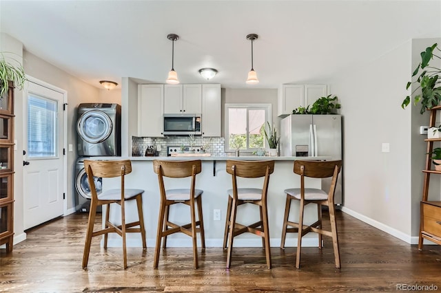 1171 Syracuse St, Denver, CO 80220 - kitchen with stainless steel appliances, estacked washer and dryer, dark wood-style floors, a breakfast bar area, and light countertops