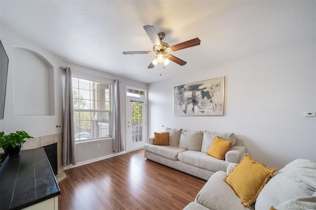 living room with a textured ceiling, dark hardwood / wood-style floors, a tile fireplace, and ceiling fan