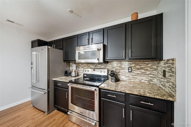 kitchen with stainless steel appliances, light stone counters, a textured ceiling, light hardwood / wood-style floors, and tasteful backsplash