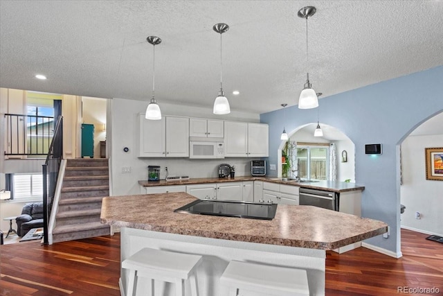 4194 S Kalispell St, Aurora, CO 80013 - kitchen with white microwave, stainless steel dishwasher, dark wood-style flooring, a textured ceiling, and arched walkways