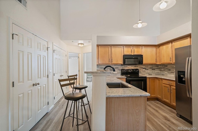 5465 Zephyr St Unit 201, Arvada, CO 80002 - kitchen with black appliances, a peninsula, light wood-type flooring, a kitchen breakfast bar, and decorative backsplash
