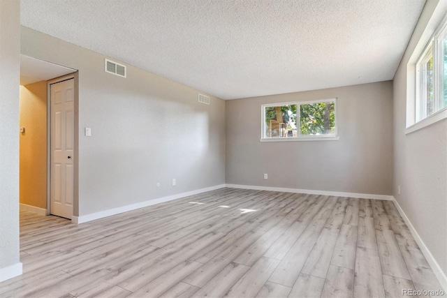 unfurnished room featuring a textured ceiling, plenty of natural light, and light hardwood / wood-style flooring