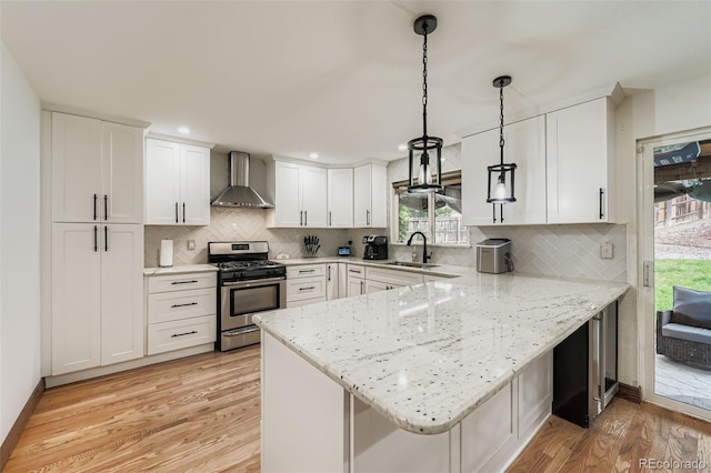 9559 Elizabeth Ct, Thornton, CO 80229 - kitchen featuring wall chimney range hood, stainless steel gas range oven, a peninsula, light wood-type flooring, and white cabinets