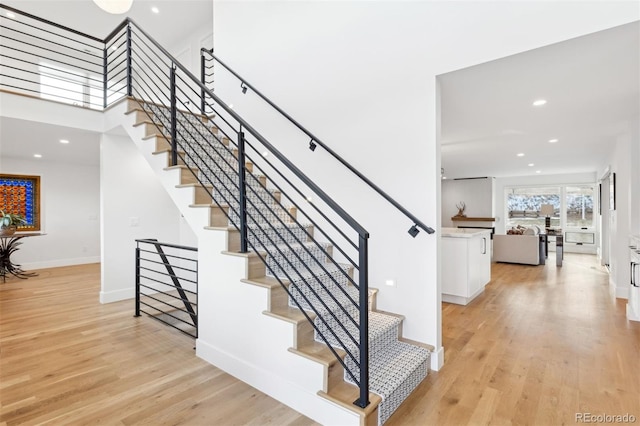 staircase featuring recessed lighting, wood finished floors, a towering ceiling, and baseboards