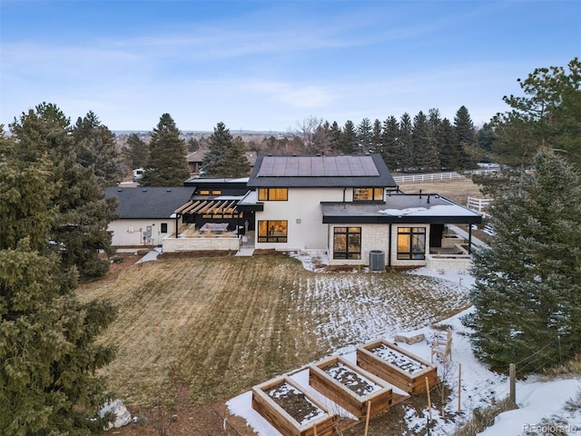 snow covered property with metal roof, central air condition unit, a garden, stucco siding, and a standing seam roof