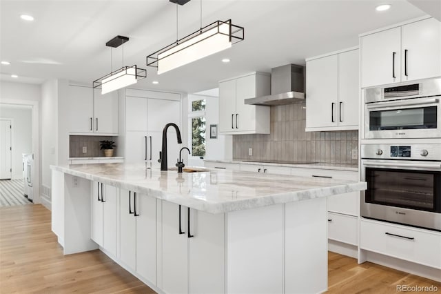 kitchen with pendant lighting, white cabinets, an island with sink, and wall chimney exhaust hood