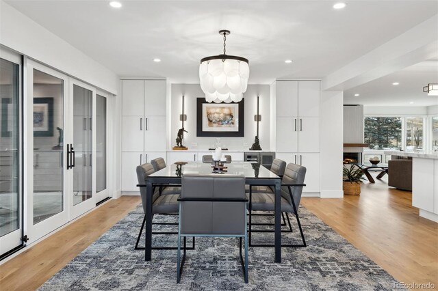 dining space featuring a warm lit fireplace, an inviting chandelier, light wood-style floors, and recessed lighting