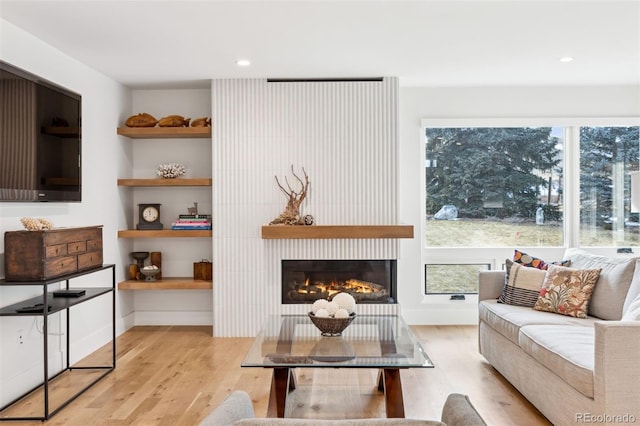 living room with recessed lighting, light wood-style flooring, and a glass covered fireplace