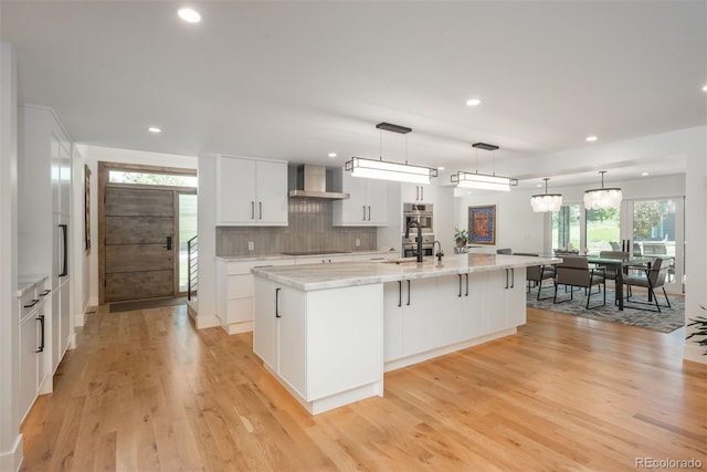 17326 W 57th Ave, Golden, CO 80403 - kitchen featuring wall chimney exhaust hood, white cabinetry, light wood-style floors, a large island with sink, and backsplash