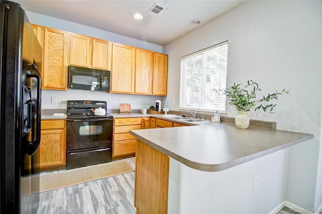 kitchen with light hardwood / wood-style flooring, sink, kitchen peninsula, and black appliances