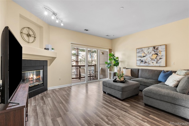 living room featuring visible vents, baseboards, wood finished floors, and a tile fireplace