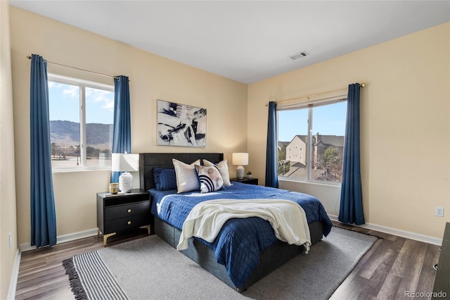 bedroom with multiple windows, wood finished floors, and baseboards