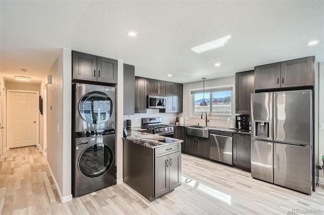 kitchen with light wood-type flooring, dark stone counters, stainless steel appliances, sink, and stacked washer / dryer