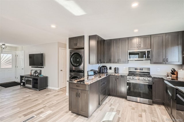 kitchen featuring stone counters, appliances with stainless steel finishes, stacked washer and dryer, and light hardwood / wood-style flooring