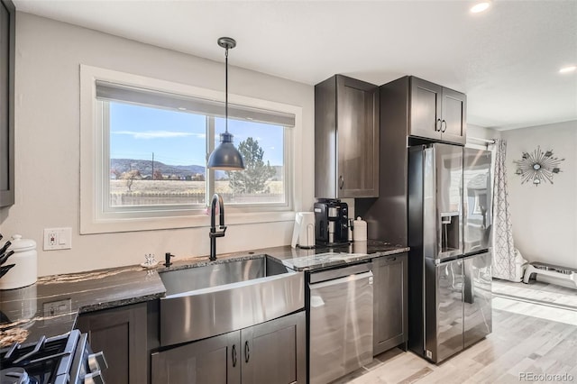 kitchen featuring sink, light hardwood / wood-style flooring, dark stone countertops, decorative light fixtures, and stainless steel appliances