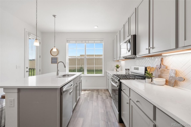 2140 Santini Trl Unit F, Littleton, CO 80129 - kitchen with appliances with stainless steel finishes, a sink, light wood finished floors, tasteful backsplash, and an island with sink