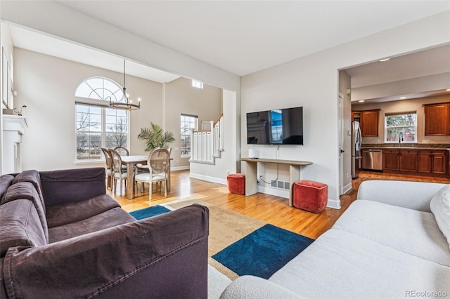 living room featuring baseboards, visible vents, light wood-style flooring, an inviting chandelier, and stairs