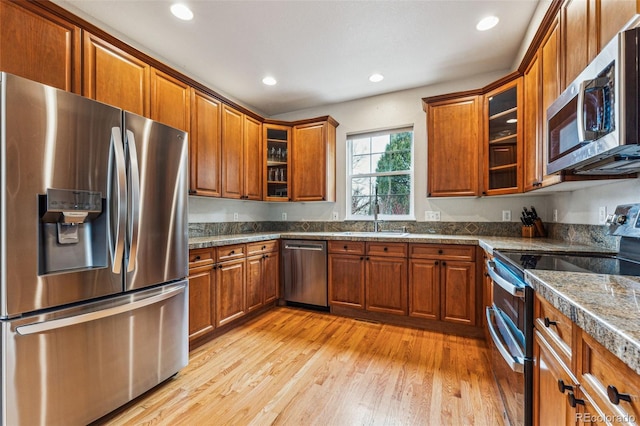 kitchen with appliances with stainless steel finishes, brown cabinets, glass insert cabinets, and a sink