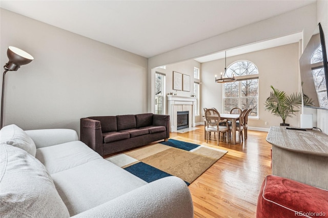 living room featuring baseboards, an inviting chandelier, a fireplace with flush hearth, and light wood-style floors