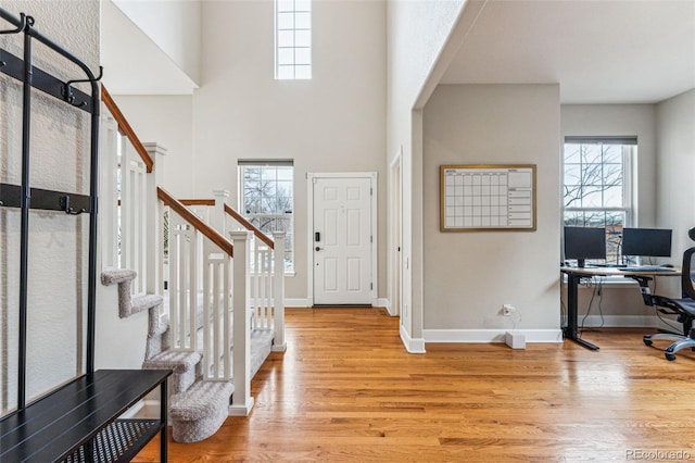 foyer entrance featuring baseboards, stairway, light wood-type flooring, and a healthy amount of sunlight