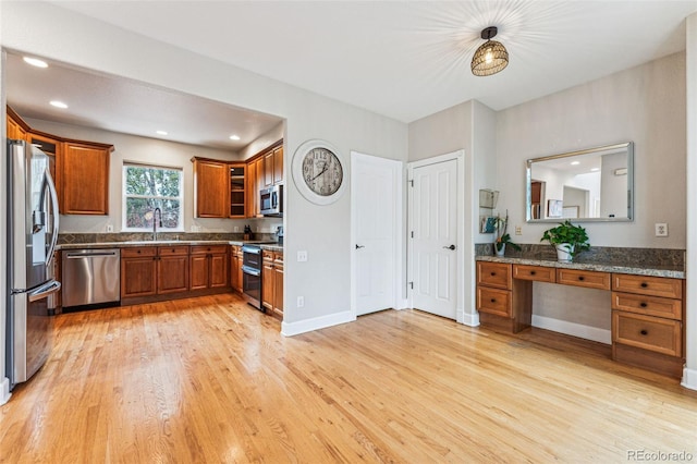 kitchen with built in study area, appliances with stainless steel finishes, brown cabinets, light wood-style floors, and a sink