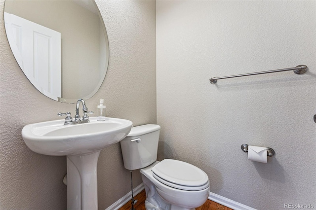 bathroom featuring baseboards, a textured wall, toilet, and wood finished floors