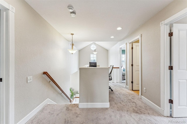 corridor with baseboards, a textured wall, light colored carpet, vaulted ceiling, and an upstairs landing