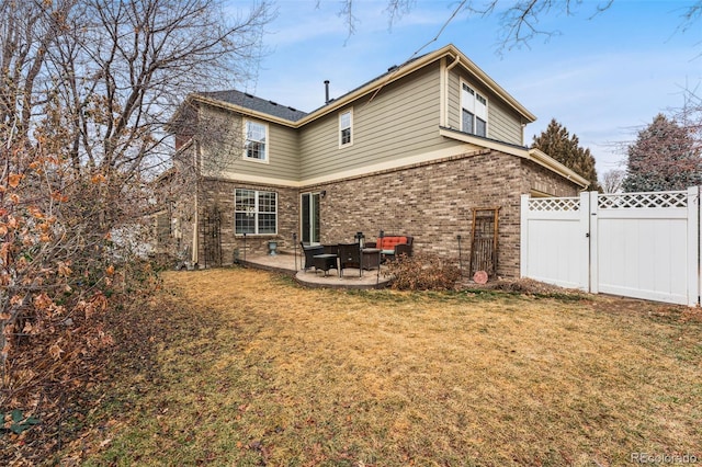 back of property with a lawn, a gate, fence, a patio area, and brick siding