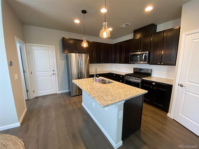 kitchen with an island with sink, sink, decorative light fixtures, appliances with stainless steel finishes, and light stone countertops