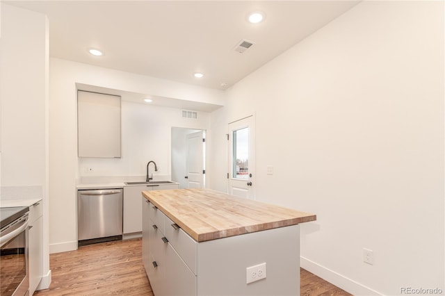 kitchen with butcher block counters, sink, white cabinetry, appliances with stainless steel finishes, and a kitchen island