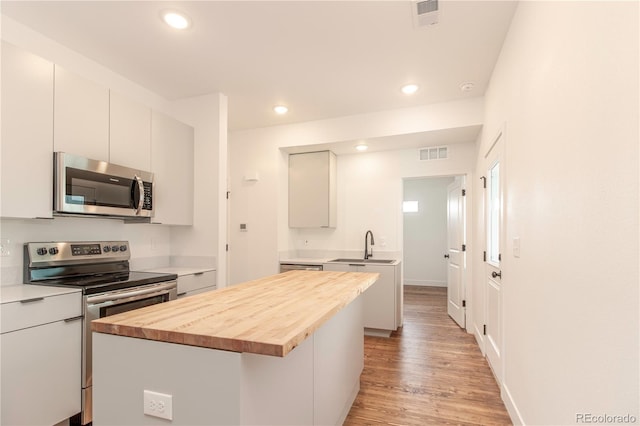 kitchen featuring a kitchen island, white cabinetry, butcher block counters, stainless steel appliances, and light hardwood / wood-style flooring