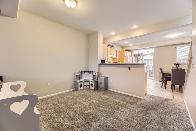 kitchen with a peninsula, light carpet, baseboards, stainless steel microwave, and under cabinet range hood