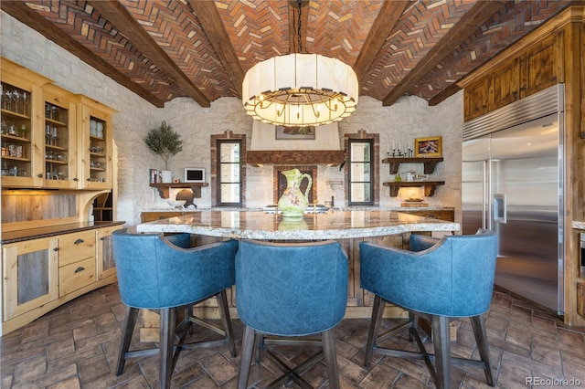 kitchen featuring stainless steel built in fridge, brick ceiling, light stone counters, and a kitchen bar