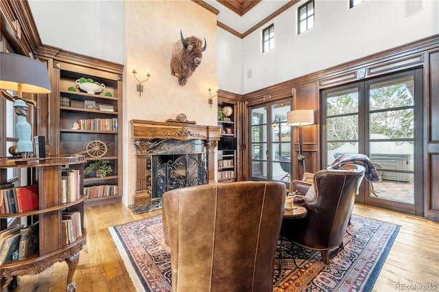 living room featuring light wood-type flooring, a high end fireplace, built in shelves, a towering ceiling, and ornamental molding