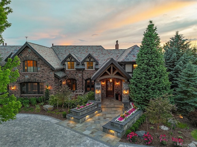view of front of home featuring a high end roof, stone siding, and a chimney