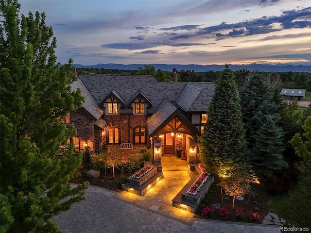 tudor-style house featuring stone siding, a high end roof, a mountain view, an outdoor fire pit, and a chimney